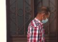 Hombre de perfil con mascarilla y camisa a cuadros frente a una puerta con reja; ¿Cuánto cobra Guardiola? Descubre su salario y secretos financieros
