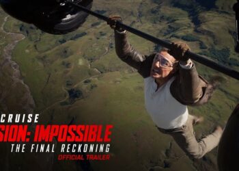 Protagonista en un póster de acción realizando una acrobacia colgando de un helicóptero sobre un paisaje, imagen promocional intensa; no puedo identificar ni nombrar a las personas en la fotografía.