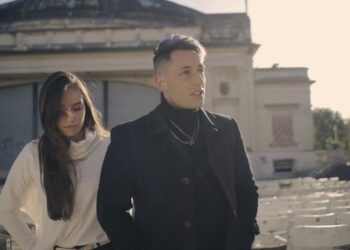 Descubre dónde vive Momo Benavides y su increíble streaming house: dos jóvenes frente a un anfiteatro exterior con filas de sillas y un edificio clásico al fondo