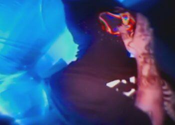 Perfil oscuro con capucha y tatuajes iluminado por efectos neón y tonos azules, Luzu: origen y trayectoria en el mundo digital