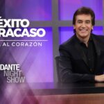 Presentador sonriente en un set de programa nocturno con fondo púrpura, micrófono retro y escritorio