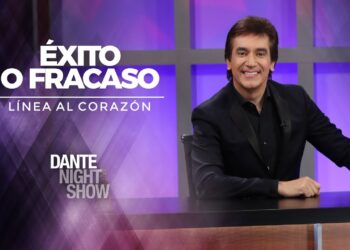 Presentador sonriente en un set de programa nocturno con fondo púrpura, micrófono retro y escritorio