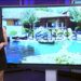 Presentadora de televisión en un plató junto a una gran pantalla que muestra una casa con piscina y jardines - Dónde vive Irene Montero: descubre su hogar en Galapagar