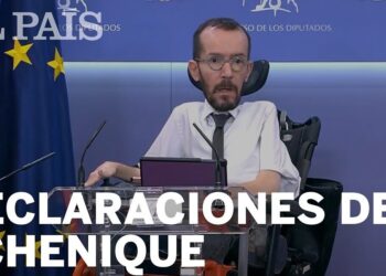 Político en silla de ruedas en un atril con banderas y micrófonos, rueda de prensa sobre declaraciones y patrimonio.