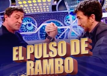 Dos hombres forcejeando en un plató televisivo con decorado luminoso y texto destacado; ¿De dónde es Pablo Motos? Descubre sus raíces y su historia