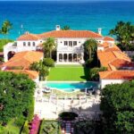 Descubre dónde vive Sylvester Stallone y su lujosa mansión: vista aérea de una residencia costera con tejados de teja roja, piscina, césped central y palmeras frente al mar.