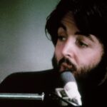 Hombre con barba cantando frente a un micrófono en un estudio íntimo en primer plano