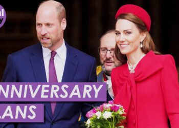 Descubre el encantador secreto de la noche de aniversario que te dejará sin aliento: una elegante pareja real sonriente, ella con abrigo rojo y ramo de flores, él con traje azul.