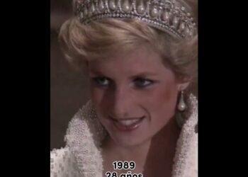 Mujer con tiara y pendientes de perla sonriendo en primer plano con un vestido ornamentado de perlas, momento emotivo