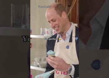 Hombre sonriente con delantal sosteniendo un cupcake con glaseado azul, mostrando un gesto amable.