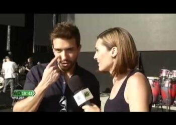 Entrevista en el escenario a un cantante durante una prueba de sonido con micrófono y percusión al fondo.