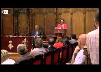 Acto institucional en el salón de plenos con una oradora en el atril frente a un público sentado.