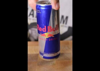 Lata de bebida energética Red Bull sostenida por una mano sobre una tabla de madera, Aczino: Descubre de dónde es el campeón del freestyle mexicano