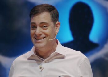 Hombre sonriente con micrófono de diadema en escenario y fondo azul con silueta
