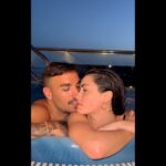 Pareja abrazada en un jacuzzi al atardecer en una terraza con barandilla y vistas al mar