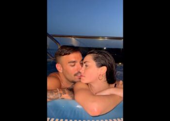 Pareja abrazada en un jacuzzi al atardecer en una terraza con barandilla y vistas al mar