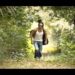 Hombre con guitarra caminando por un sendero selvático, gafas de sol y ropa casual, descubre sus raíces guatemaltecas y su historia.