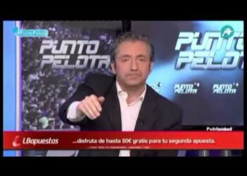 Presentador de programa deportivo en plató con rótulos luminosos y gesto serio, ambiente de debate televisivo