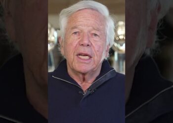 Hombre mayor con cabello blanco hablando frente a la cámara durante una aparente conferencia de prensa en un interior elegante.