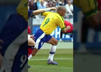 Delantero con camiseta amarilla número 9 corriendo en el área mientras un defensor lo sujeta en un partido de fútbol