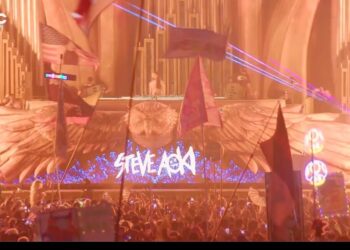 Concierto nocturno con gran multitud frente a un escenario iluminado y el texto ¿De dónde es Steve Aoki? Descubre sus raíces y su historia visible en la pantalla