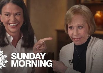 Dos mujeres sonrientes posan en una entrevista con el logo 'SUNDAY MORNING', deslumbrantes en la alfombra roja con sonrisas radiantes.