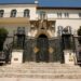La casa de Versace: descubre el lujo y la historia de su mansión con un portón ornamental de hierro y escalones de piedra frente a una fachada mediterránea.