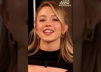 Mujer rubia sonriente en primer plano con pendientes dorados y vestido negro con abertura y transparencia, imagen que causa controversia en evento de empoderamiento femenino