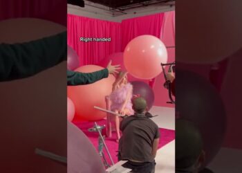 Modelo sentada en una sesión fotográfica con vestido rosa de plumas, grandes globos y equipo de producción en un set rosa