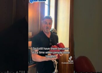 Hombre sosteniendo guantes de boxeo rojos frente a una estantería en un interior con subtítulos visibles