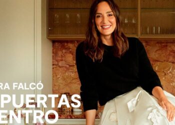 Mujer sonriente sentada sobre una encimera de cocina con respaldo de mármol y mobiliario elegante, luz cálida y estilo contemporáneo.