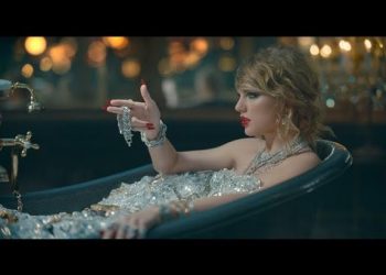 Mujer elegante recostada en una bañera llena de joyas y cristales, mirada intensa y labial rojo; Mandy Moore revela cómo su nuevo show la hace sentir como Taylor Swift y tú no te lo querrás perder