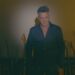 Hombre de pie en un estudio oscuro frente a una fila de guitarras; ¿De dónde es Alejandro Sanz? Descubre sus raíces andaluzas
