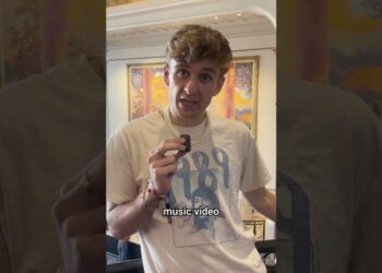 Joven con camiseta 1989 sosteniendo un dispositivo frente a una pintura, Descubre todos los secretos ocultos en el video musical de Taylor Swift que te dejarán boquiabierto