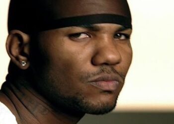 Primer plano de un hombre con paño negro en la cabeza, pendiente y expresión seria mirando de reojo.