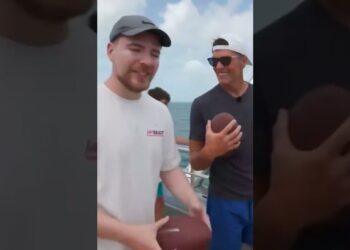 Dos hombres sonrientes en la cubierta de un barco sosteniendo balones de fútbol americano en una escena relajada; ¿Cuánto cobra Tom Brady? Descubre su impresionante fortuna y más