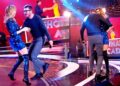 Presentadores y parejas bailando en un estudio de televisión con escenario iluminado y vestuario brillante