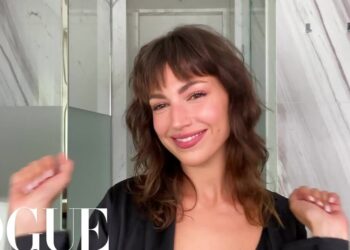 Mujer sonriente en un baño con paredes de mármol y espejo, imagen descriptiva sin identificación de la persona.