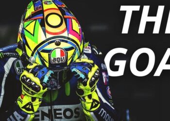 Casco colorido y guantes de un piloto de motociclismo junto al texto 'THE GOAT' que sugiere grandeza