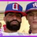 Primer plano de dos hombres con gorras deportivas azules y rojas, uno con barba, posando juntos en un entorno público