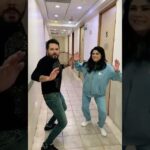Dos personas en un pasillo de hotel o edificio, levantando las manos como si bailaran o posaran para un video