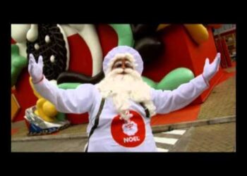 Persona vestida de Papá Noel en un desfile navideño con los brazos abiertos; Descubre dónde vive Papá Noel y los secretos de su hogar mágico.