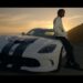 Hombre apoyado en un coche deportivo blanco con franjas negras al atardecer; ¿Cuánto dinero tiene Wiz Khalifa? Descubre su impresionante fortuna
