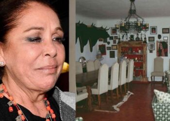 Retrato de una mujer junto a un salón comedor con mesa larga, lámpara de araña, sillas de respaldo alto y muebles tapizados