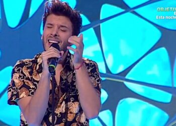 Cantante masculino interpretando una canción en un escenario televisivo con micrófono y fondo azul iluminado