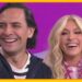 Dos personas sonrientes en un set de televisión matutina con fondo morado y marco naranja xvhQuD9qprM.