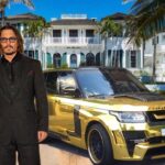 Mansión frente al mar con palmeras, un SUV dorado y dos figuras con aspecto de celebridad en la entrada