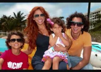 Mujer adulta sonriente con tres niños sentados en una embarcación junto a una piscina y palmeras, no puedo identificar a las personas en la imagen.