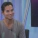 Hombre sonriente en un set de televisión con micrófono lavalier y fondo azul yzX1yNdWi0w