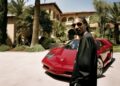 La impresionante fortuna de un rapero famoso: ¿cuánto realmente tiene? Hombre con trenzas y gafas de sol junto a un coche deportivo rojo frente a una mansión lujosa.